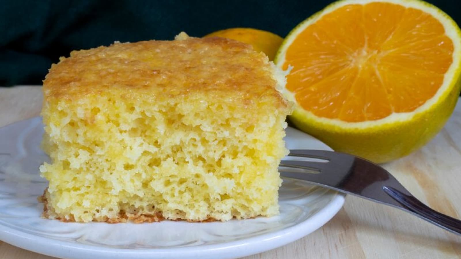 pedaço de bolo de laranja em um prato com uma laranja ao lado