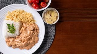 Estrogonofe em prato branco acompanhado de arroz, batata palha, champignons e tomate