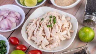 Frango desfiado em tigela branca perto de tomate, limão e outros ingredientes