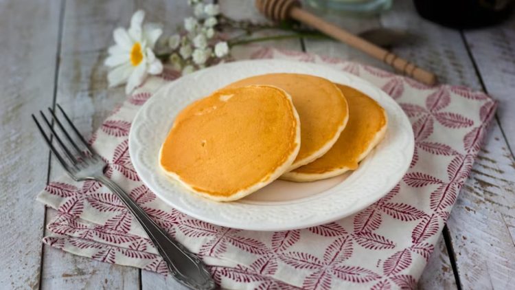 panquecas em prato branco sobre pano ao lado de talheres e flores