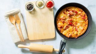 Pizza de frigideira ao lado de utensílios de cozinha e ingredientes