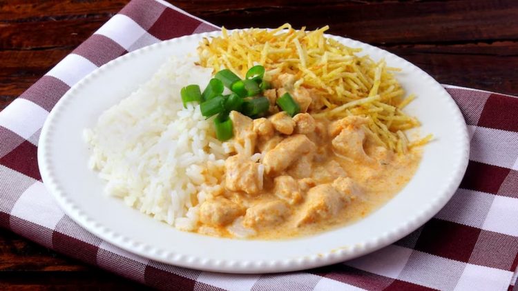 Strogonoff de frango com arroz e batata palha em prato branco sobre toalha xadrez