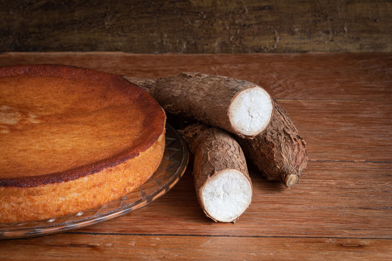 bolo de mandioca ralada redondo com 3 mandiocas ao lado